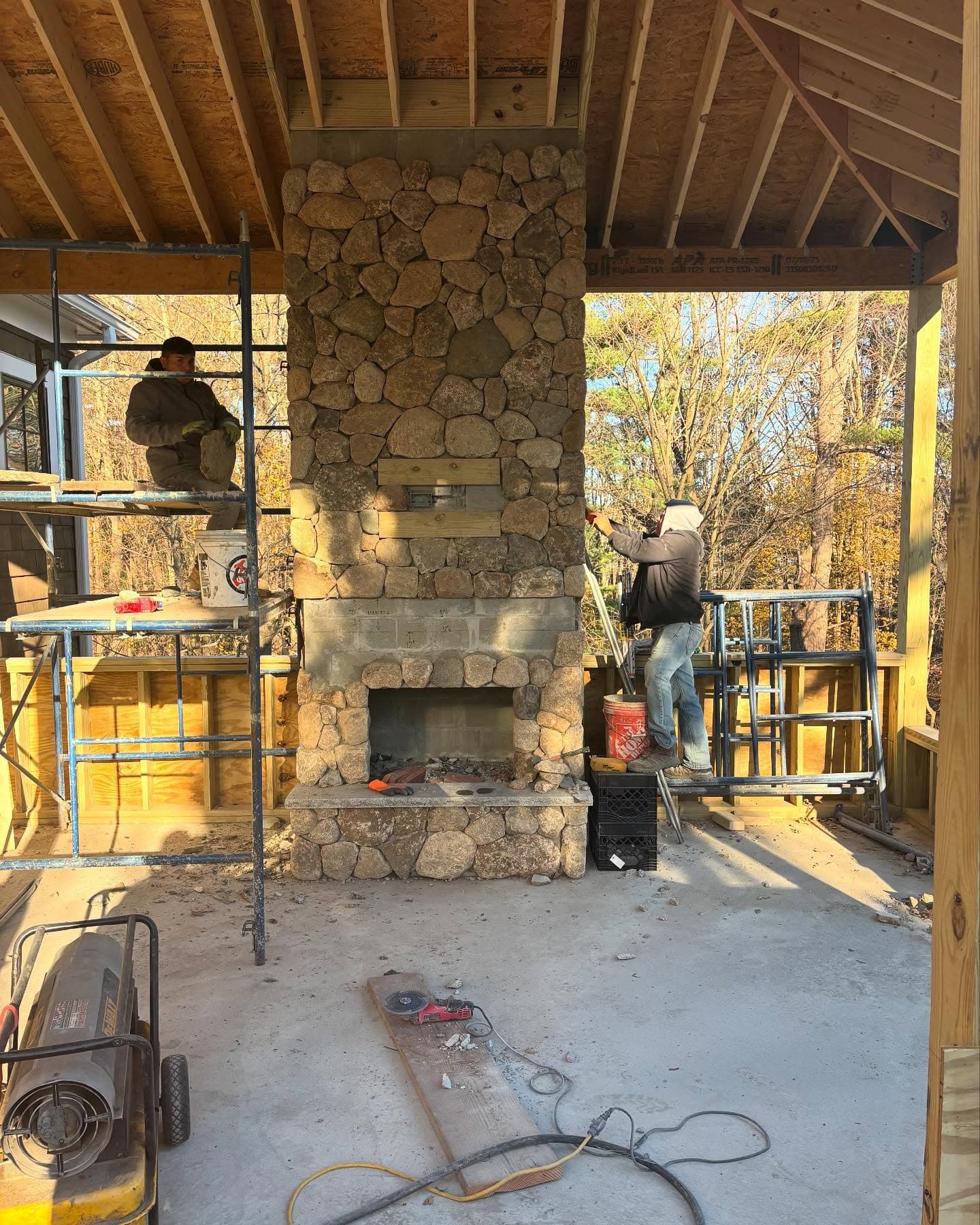 Mason building a fieldstone fireplace on a covered porch, on scaffolding