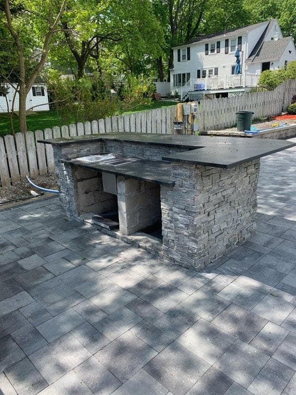 Stacked-stone grill island with a black granite top on a paver patio
