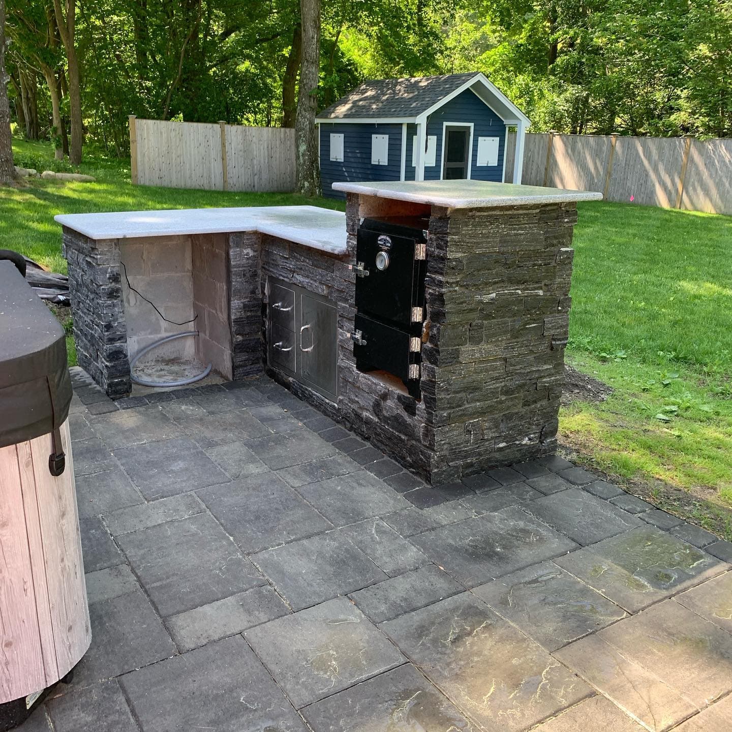 L-shaped stone outdoor kitchen on a paver patio