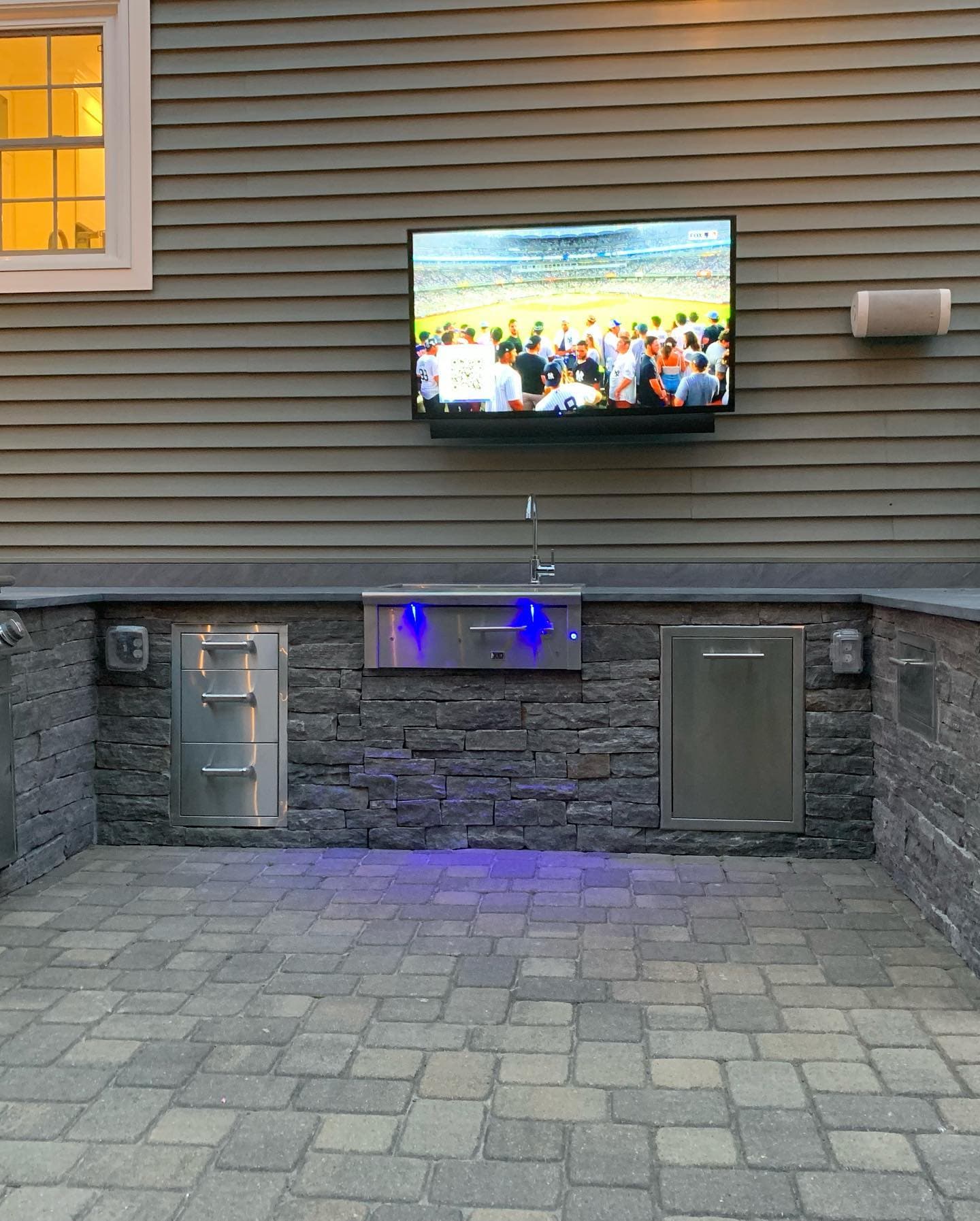 Outdoor kitchen with lit drawers under a TV