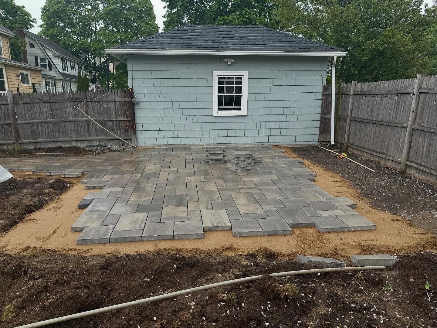 Crew laying pavers on a screeded bed in front of a shed