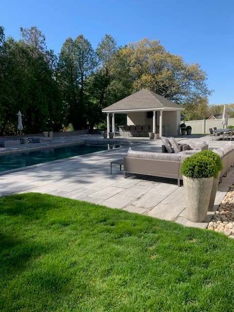 Paver patio and lawn beside a pool and pool house