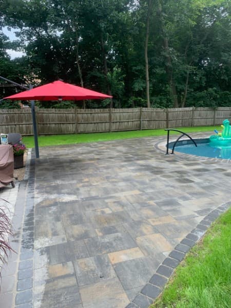 Paver patio with an umbrella and seating next to a pool