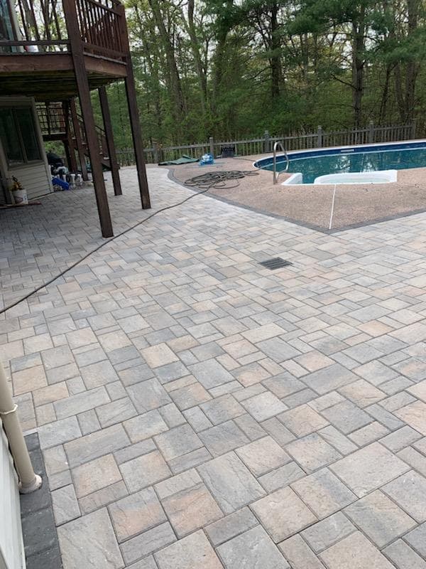 Paver patio under a deck leading out to a pool