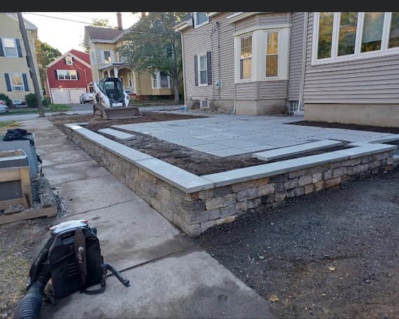 Raised stone-walled patio with bluestone caps under construction in Salem