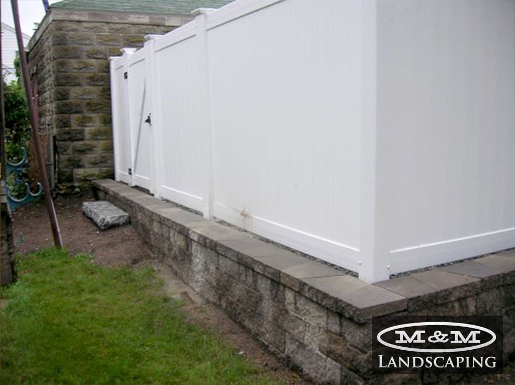 White vinyl privacy fence on top of a low stone wall