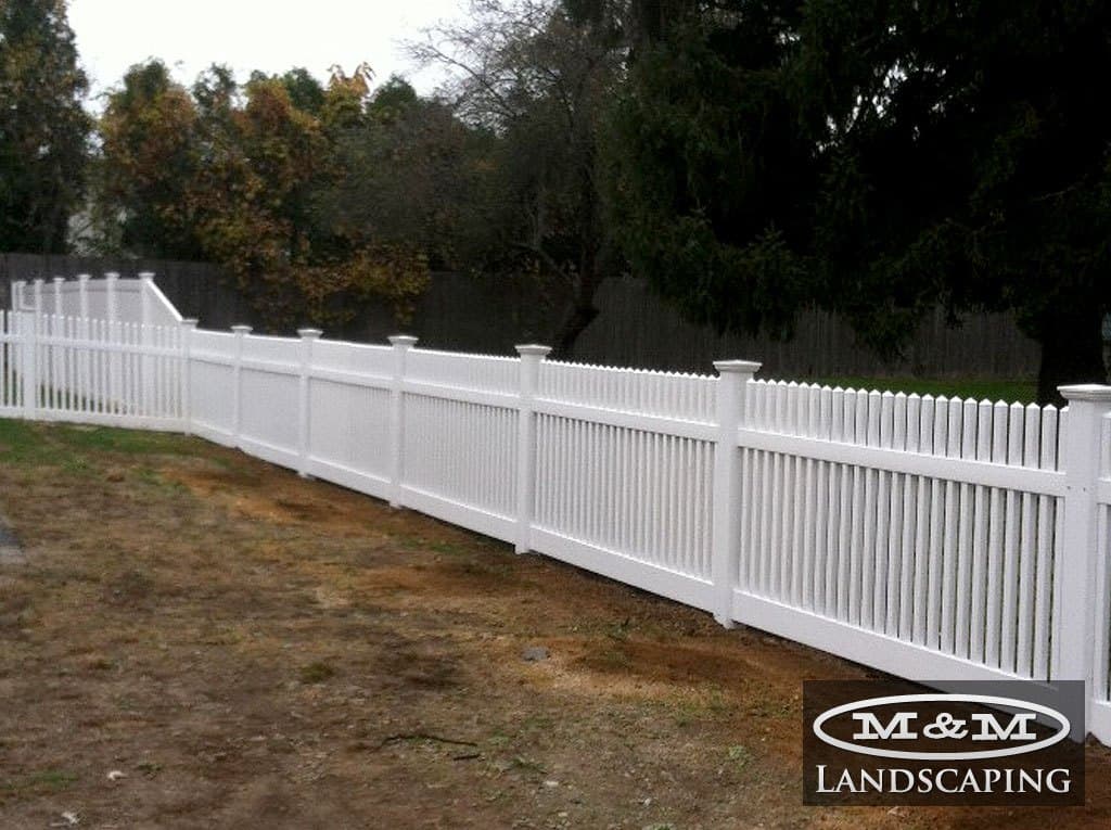Long white vinyl picket fence following a slope