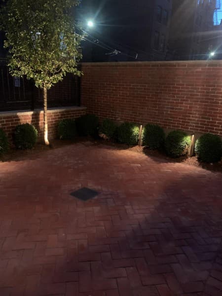 Brick courtyard at night with low lights along the planting beds