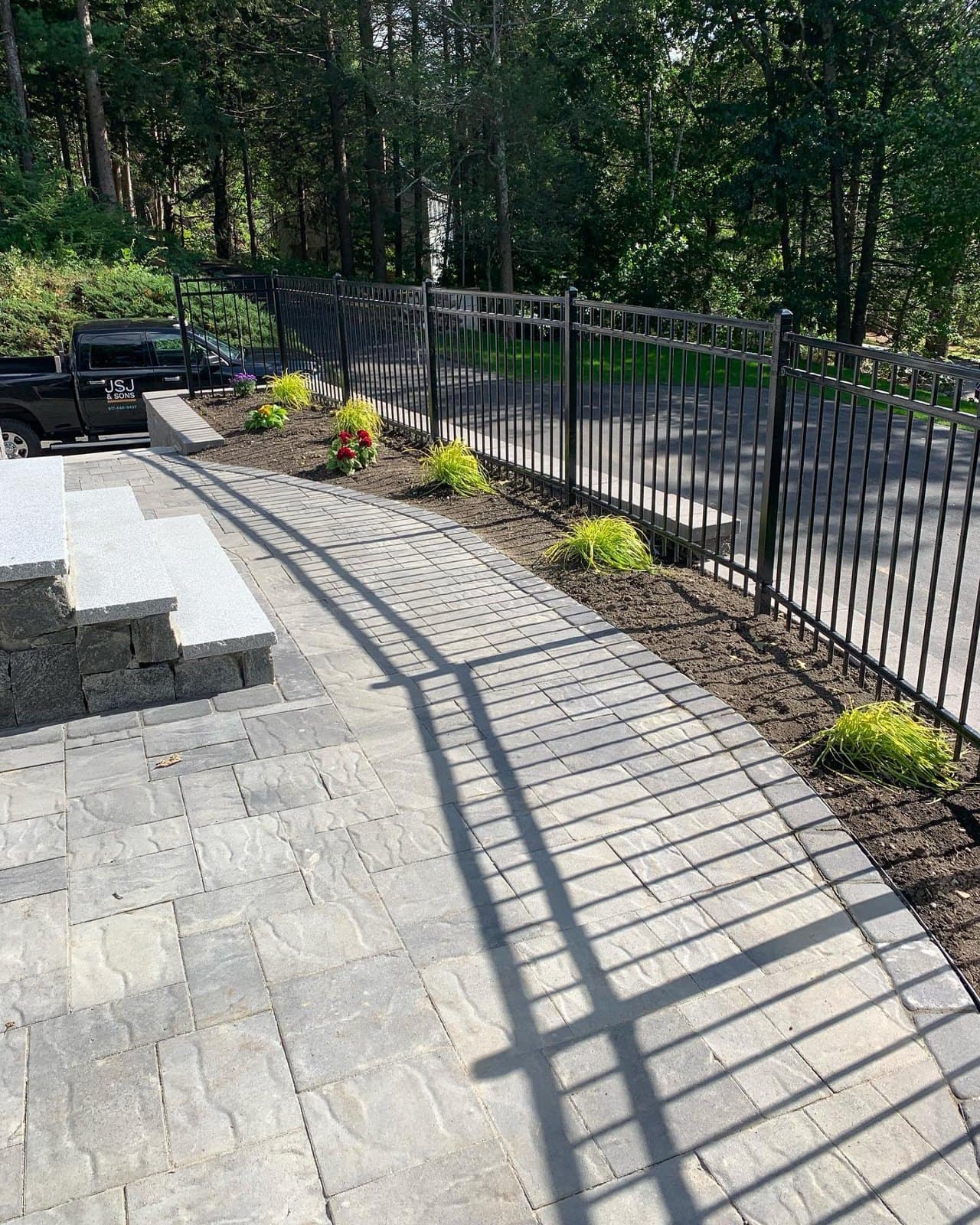 Long paver walkway with steps along a black metal fence